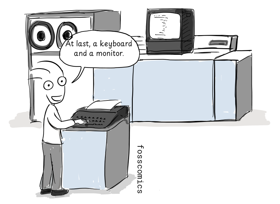 A smiling programmer uses a keyboard beside a large computer with tape reels, a display, and a printer.